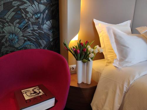 une chaise rouge et un vase de fleurs dans une chambre d'hôtel dans l'établissement Dali Hôtel Perpignan - Restaurant, à Perpignan