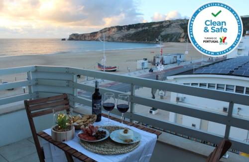 einen Tisch mit Weingläsern und Speisen auf einem Balkon mit Strand in der Unterkunft Beachfront Apartment Nazaré in Nazaré