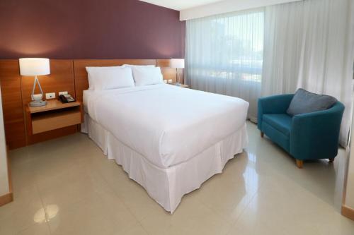 - une chambre avec un grand lit blanc et une chaise bleue dans l'établissement Staybridge Suites Guadalajara Expo, an IHG Hotel, à Guadalajara