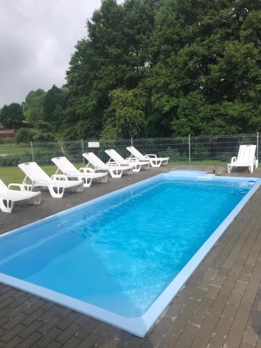 una piscina con tumbonas blancas y una piscina azul en Hotel Rezydencja Mazury SPA & Lake, en Mrągowo