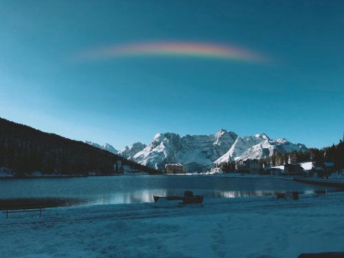 a lake with a bench and snow covered mountains at Quinz - Locanda Al Lago in Misurina