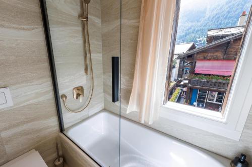 ducha con puerta de cristal y ventana en Hotel Derby, en Zermatt