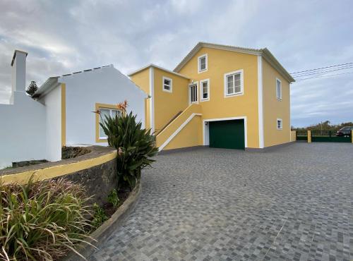 une maison jaune avec un garage dans une allée dans l'établissement CASA do CAMINHO, à Praia da Vitória