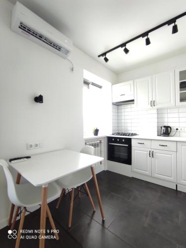 een keuken met witte kasten en een witte tafel en stoelen bij White Apartment in Poltava