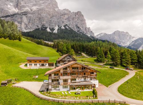 uma casa numa colina com montanhas ao fundo em Hotel Ciasa Rü Blanch em San Cassiano