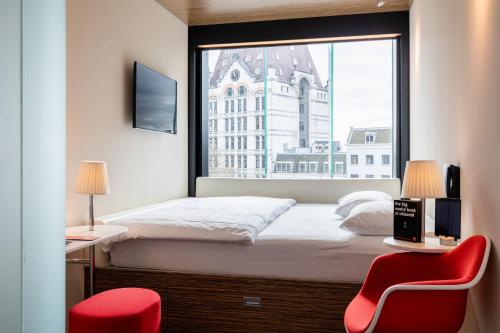 een slaapkamer met een bed met een raam en 2 rode stoelen bij citizenM Rotterdam in Rotterdam