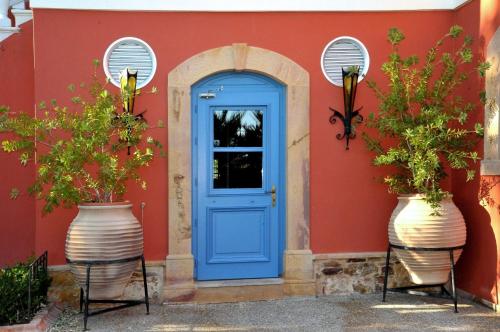 une porte bleue sur une maison rouge avec deux grands vases dans l'établissement Sourediko, à Kambos