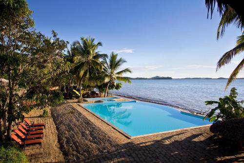 een zwembad naast de oceaan met palmbomen bij Anjiamarango Beach Resort in Nosy Be