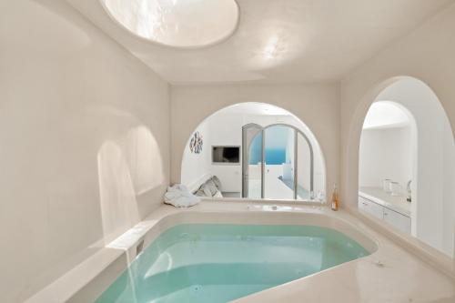 a white bathroom with a tub with a round mirror at Oyster Luxury Suites in Imerovigli