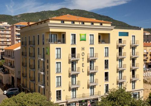 アジャクシオにあるibis Styles Ajaccio Napoleonのバルコニー付きの大きな建物で、山を背景に望めます。