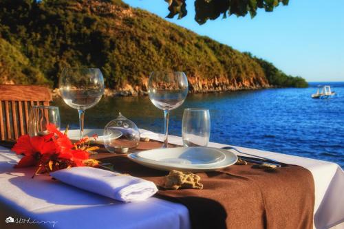 - une table avec des verres à vin et une table avec vue sur l'eau dans l'établissement Hotel Océan Beach Sakatia, à Nosy Be