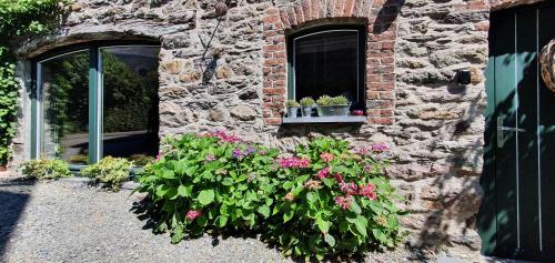 un edificio in pietra con fiori davanti a una finestra di O Près de la Lienne, maison de campagne de charme, accord parfait entre confort et authenticité a Lierneux