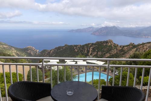 uma varanda com uma mesa e cadeiras e o oceano em Hôtel Capo Rosso em Piana