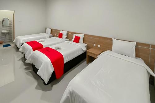 Cette chambre comprend 3 lits avec des draps rouges et blancs. dans l'établissement RedDoorz Premium @ Griya Inkoppabri Cisarua Puncak, à Bogor