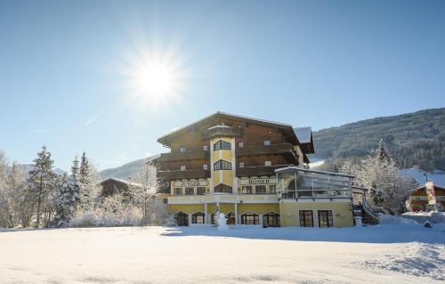 un grande edificio nella neve con il sole dietro di Hotel Zum Jungen Römer a Radstadt