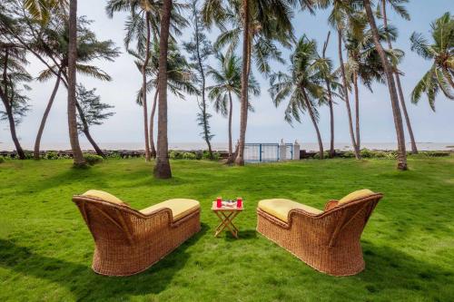 2 Stühle und ein Tisch auf einem Feld mit Palmen in der Unterkunft StayVista's Villa Bharat - Beachfront serenity with A spacious lawn in Mumbai