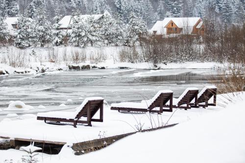 uma fila de bancos cobertos de neve junto a um rio em KLEN Family em Mykulychyn