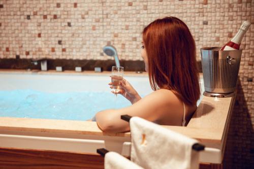 a woman sitting in a bath tub holding a glass of wine at Elexus Apartments Poiana Brasov in Poiana Brasov