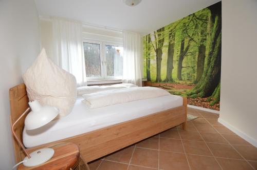 Schlafzimmer mit einem Bett und einem Wandbild von Bäumen in der Unterkunft Ferienwohnungen Rothaarglück in Schmallenberg