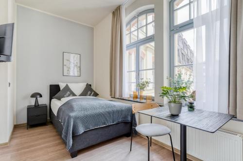 a bedroom with a bed and a table and windows at limehome Leipzig Oelßner's Hof in Leipzig