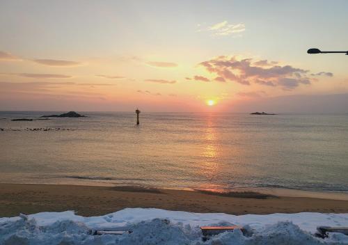 um pôr do sol na praia com um farol na água em Seaside Minbak em Goseong