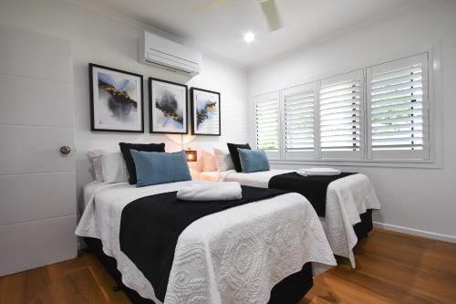 two beds in a room with white walls and windows at Birds 'n' Bloom Cottages in Yungaburra