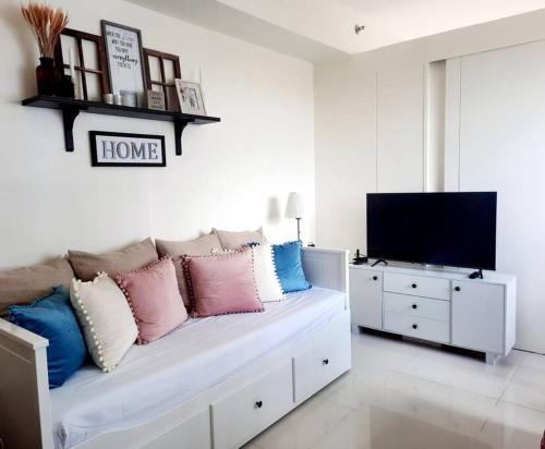 a living room with a bed with pillows and a tv at 1 BR Cozy Farmhouse-Style Condo with Balcony & Taal View at Wind Residences in Tagaytay