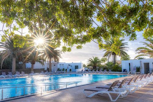 a swimming pool with lounge chairs and palm trees at Casas Heddy, Well-being Resort in Puerto del Carmen