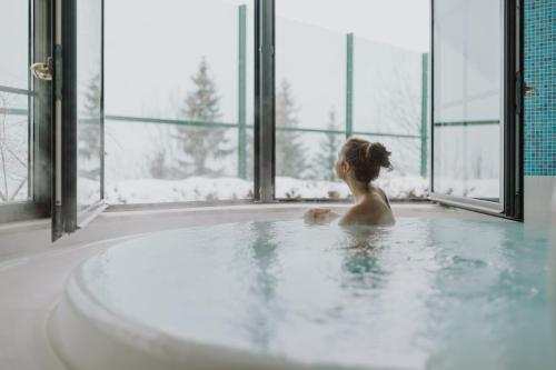 a woman in a bath tub in a room with windows at Hotel Berghof - St Johann in Salzburg in Sankt Johann im Pongau