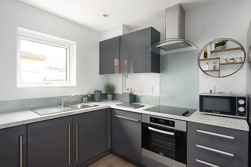 uma cozinha com armários cinzentos, um lavatório e uma janela em Stylish Serviced Apartment in Reading em Reading