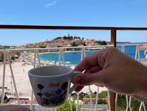 uma mão segurando uma xícara de café com vista para a praia em Rooms 22 - Beachfront em Primošten