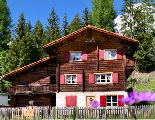 een houten huis met rode deuren en een hek bij Sonniges Chalet Arosa für 6 Pers alleinstehend mit traumhaftem Bergpanorama in Langwies