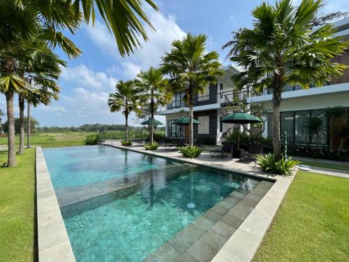 a swimming pool in front of a house with palm trees at The Valerian Villa Ubud in Ubud