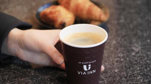 una persona sosteniendo una taza de café en un mostrador en Via Inn Shin Osaka, en Osaka