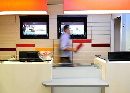 un hombre caminando detrás de un mostrador en un restaurante de comida rápida en ibis Lyon Est Beynost, en Beynost