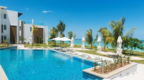 a swimming pool with chairs and umbrellas and the ocean at Cap Ouest by Horizon Holidays in Flic-en-Flac