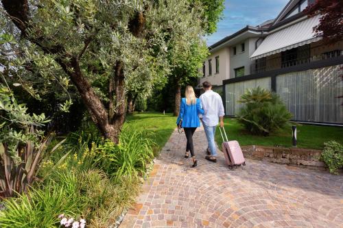 Ein Mann und eine Frau, die mit Gepäck einen Ziegelsteinweg hinuntergehen. in der Unterkunft Like Home Boutique Hotel in Azzano San Paolo