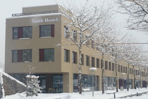 un edificio con nieve en el suelo delante de él en Interlaken Youth Hostel, en Interlaken