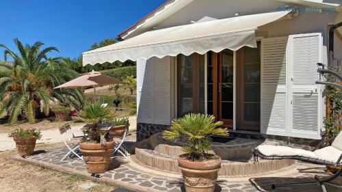 a house with a porch with chairs and an umbrella at Villetta I Due Pini - ArgonautiVacanze in Capoliveri