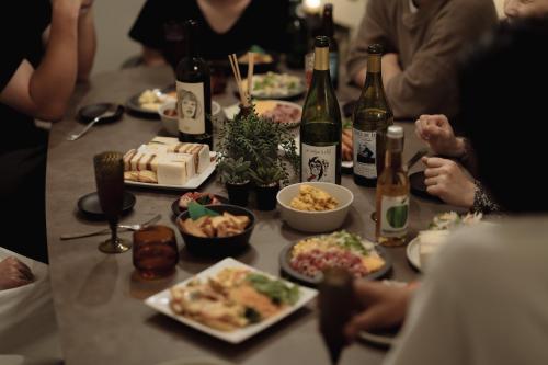 een groep mensen die rond een tafel zitten met eten en wijn bij Good Neighbors in Kanazawa