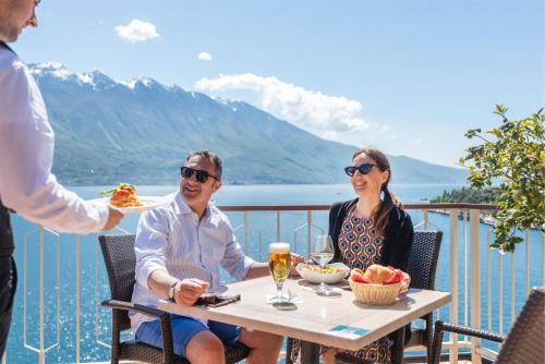 un uomo e una donna seduti a un tavolo su un balcone di Hotel Splendid Palace a Limone sul Garda