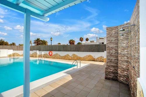 - une piscine avec un mur en briques à côté d'un bâtiment dans l'établissement Mar Azul Corralejo- Adults Only, à Corralejo