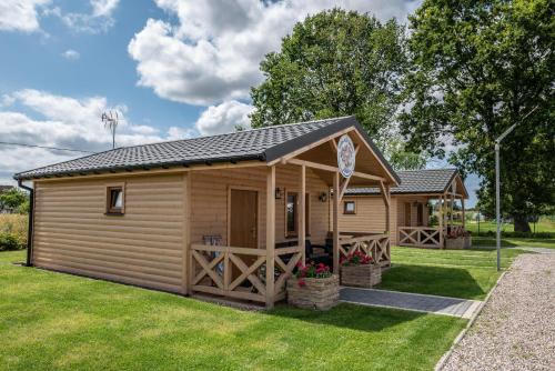 eine Holzhütte mit einer Veranda auf einem Rasen in der Unterkunft Osada Trzy Siostry in Pobierowo