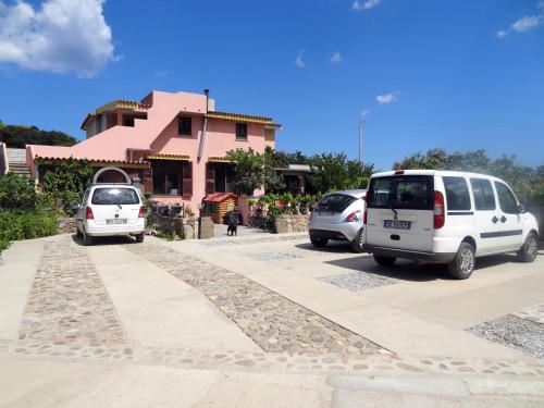 due auto parcheggiate in un parcheggio di fronte a una casa rosa di Casa Li Multi a Budoni