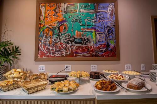 a buffet of food on a table with a painting at Hotel Cassino Tower São José do Rio Preto by Nacional Inn in Sao Jose do Rio Preto