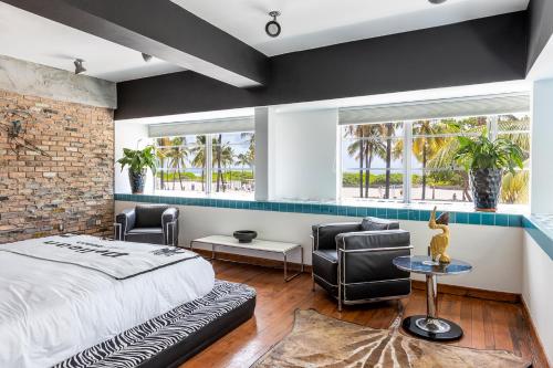 a bedroom with a bed and two chairs and two windows at Pelican Hotel in Miami Beach