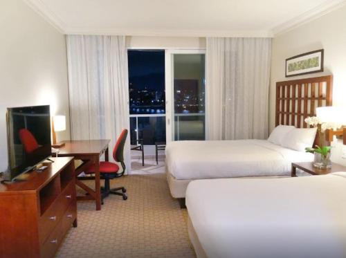 a hotel room with two beds and a desk and a television at Costa Bahia Hotel Paseo Caribe in San Juan