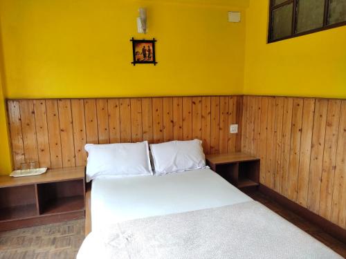 een slaapkamer met een bed en een gele muur bij Hotel Mhelung in Darjeeling