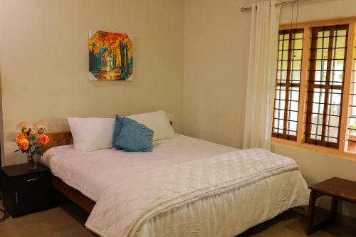 a bedroom with a bed with white sheets and blue pillows at Wayal Wayanad Heritage villa in Panamaram