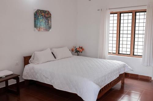 a bedroom with a large bed with white sheets and a window at Wayal Wayanad Heritage villa in Panamaram